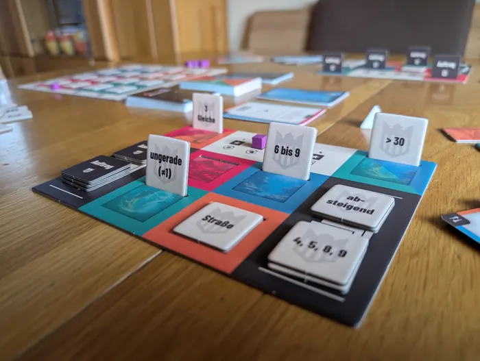 Eine Auftragstafel mit aufgestellten Auftragsplättchen wie „6 bis 9“, „ungerade“, „Straße“ und „3 Gleiche“.