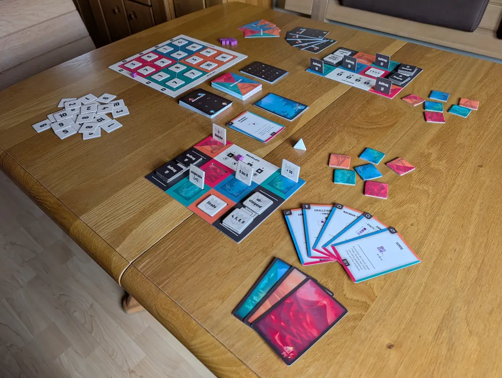 Aufgebautes Quadranti auf einem Holztisch: Spielbrett mit Zahlenchips, Kartenstapel, zwei Auftragstafeln und Handkarten.